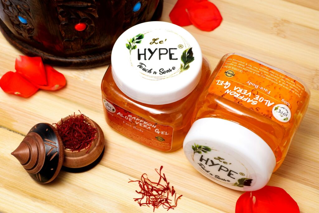 Close-up of saffron aloe vera gel jars with decorative saffron threads and petals on a wooden surface. derma product