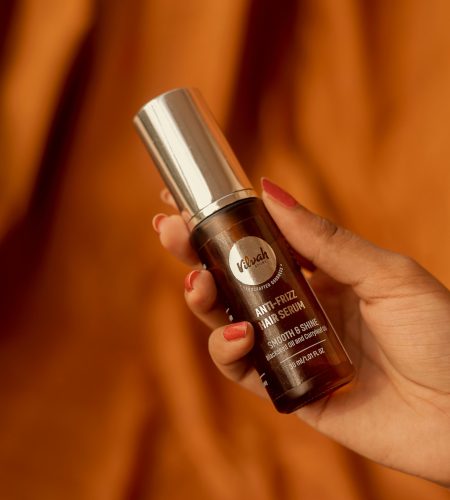 Hand holding a bottle of anti-frizz hair serum against a warm backdrop.