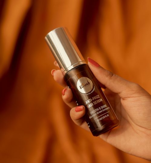 Hand holding a bottle of anti-frizz hair serum against a warm backdrop.