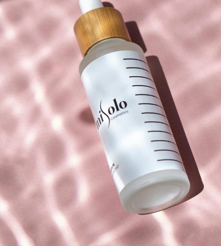 Elegant serum bottle with bamboo cap on textured pink background, emphasizing natural beauty.
