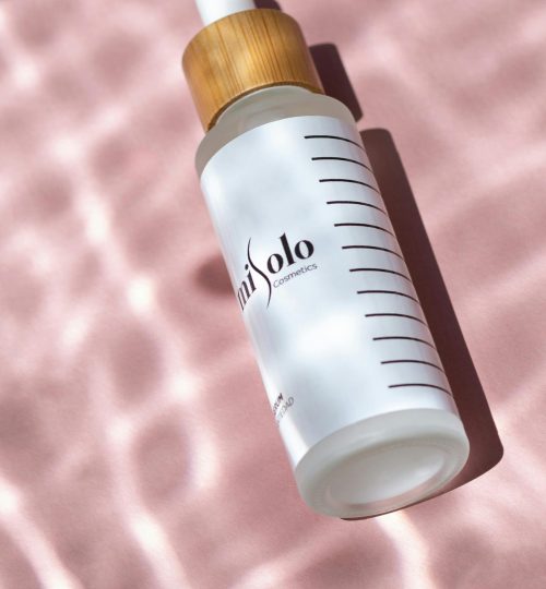 Elegant serum bottle with bamboo cap on textured pink background, emphasizing natural beauty.